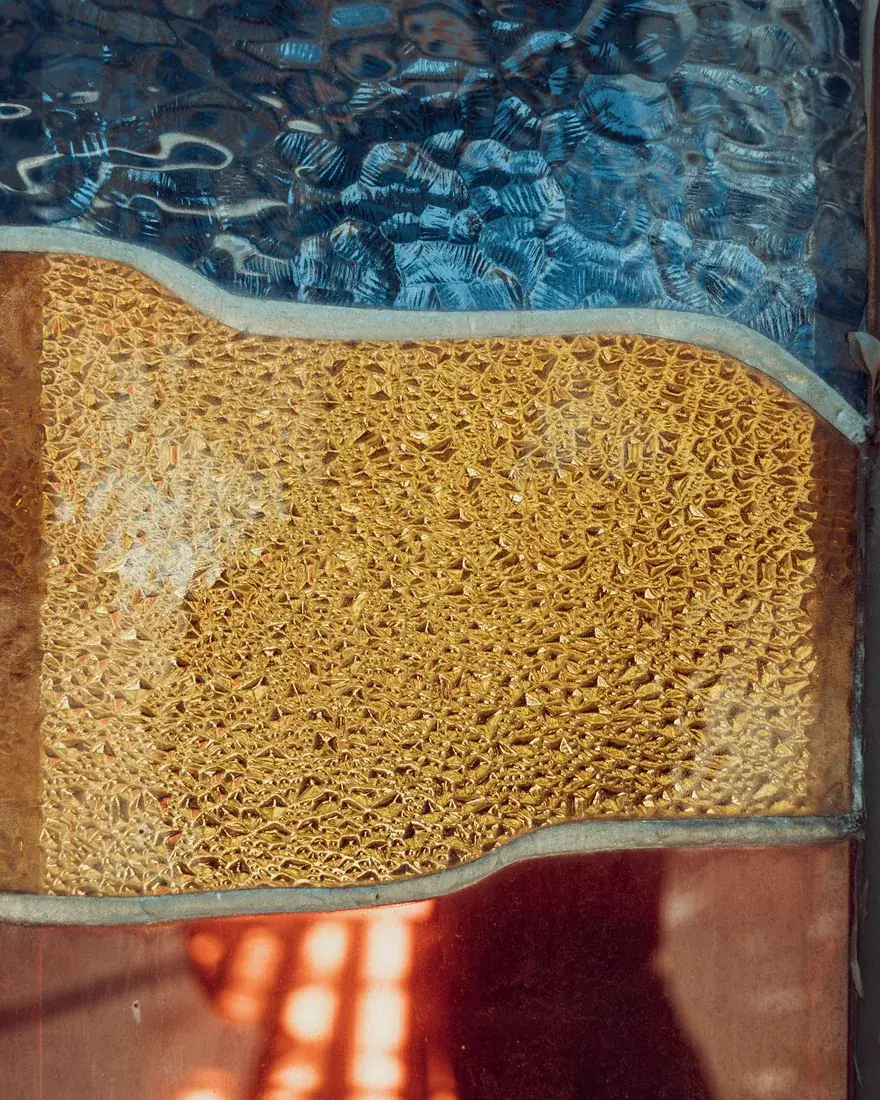 Detalle de vidrios de color con textura superficial en tonos ámbar y azul, atravesados por la luz